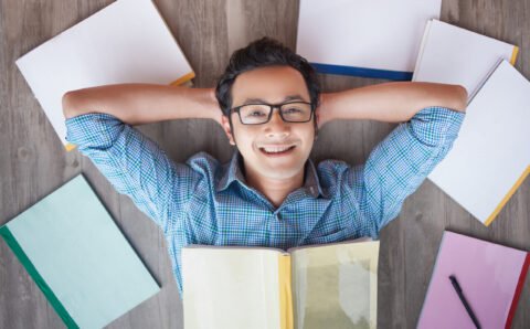 Happy Asian student boy lying on floor among books